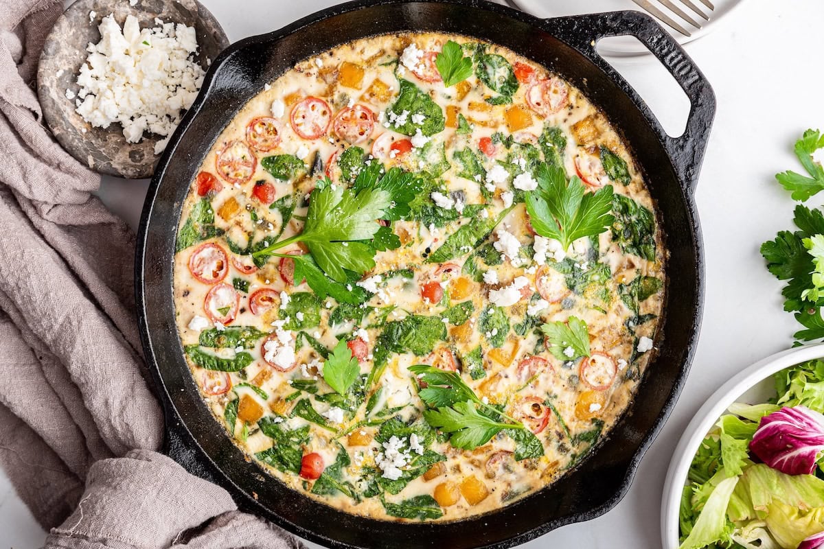 An egg white frittata in a cast iron skillet. The frittata is garnished with fresh herbs and feta cheese.