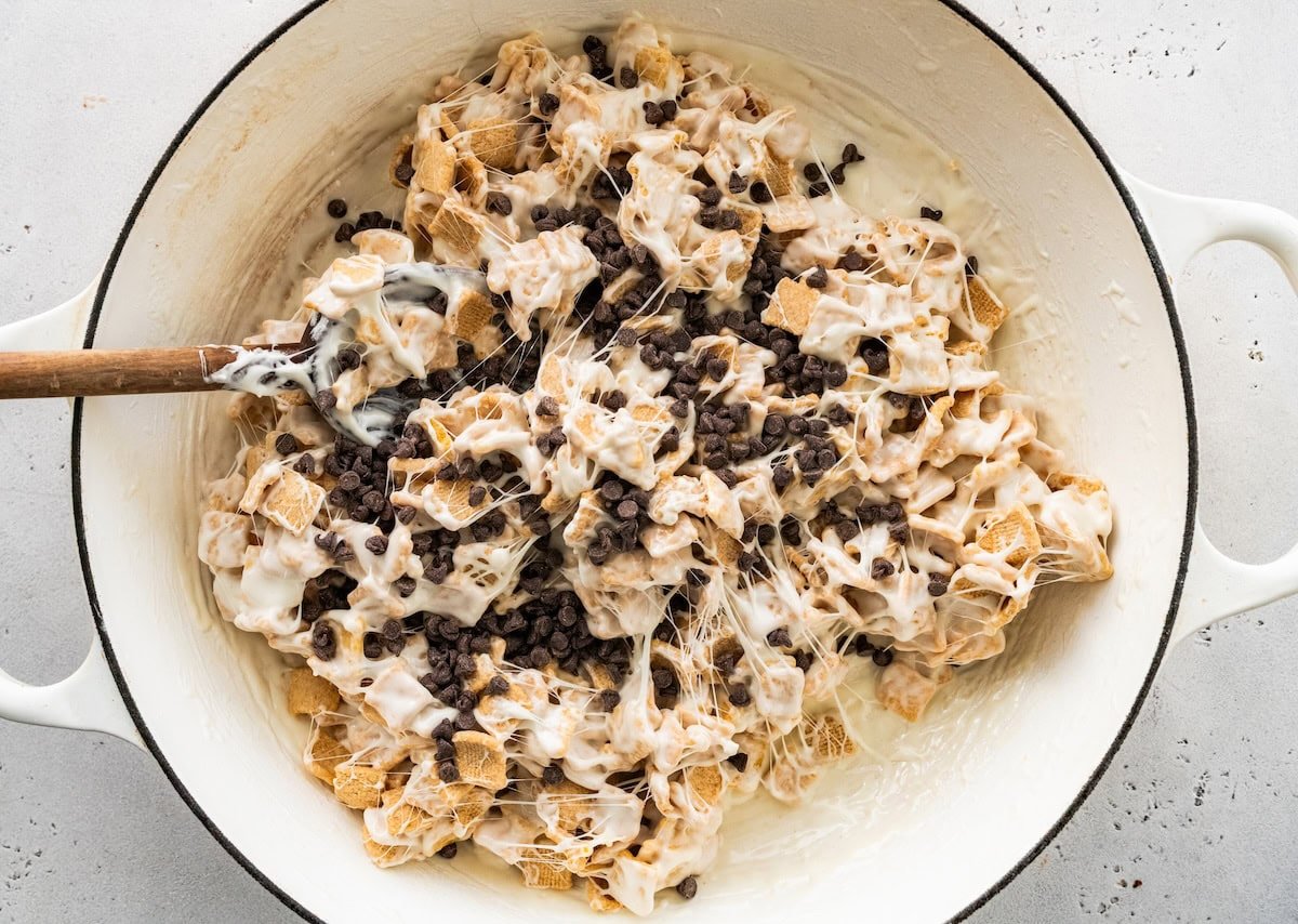 A mixture of melted marshmallows, cereal, and mini chocolate chips in a large pot.