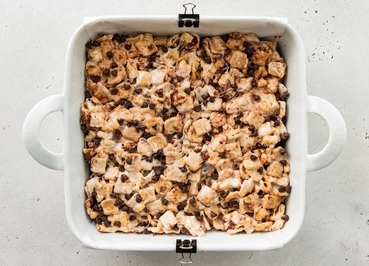 Cereal, melted marshmallow, and mini chocolate chips in a square baking dish.
