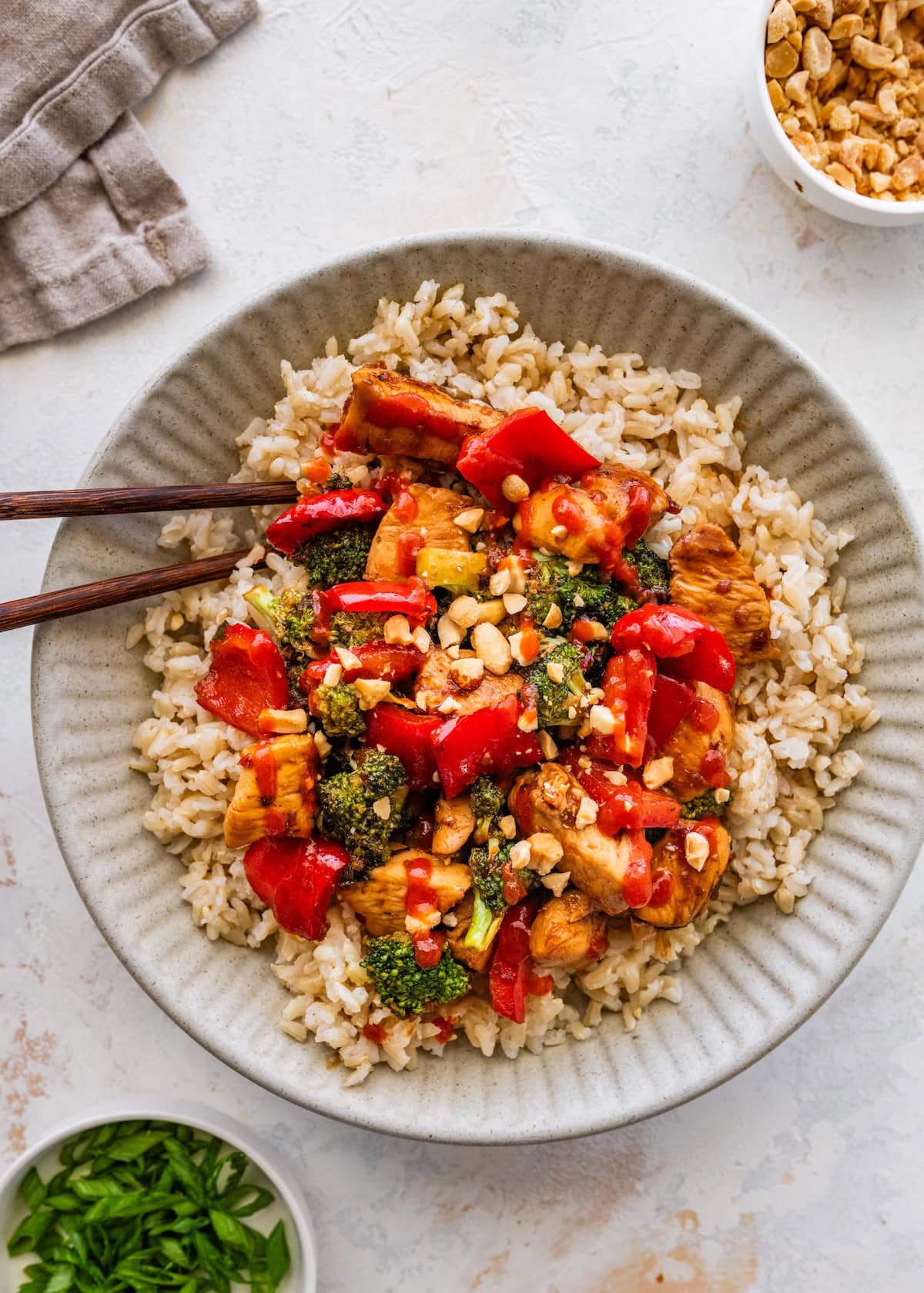 Healthy kung pao chicken served over brown rice in a shallow bowl.
