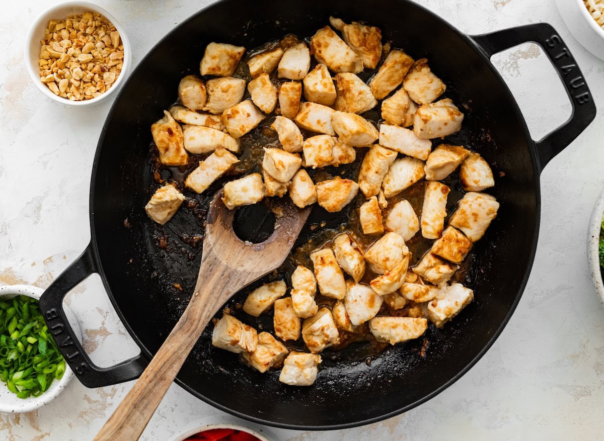 Diced chicken breast cooking in a skillet until golden and cooked through.