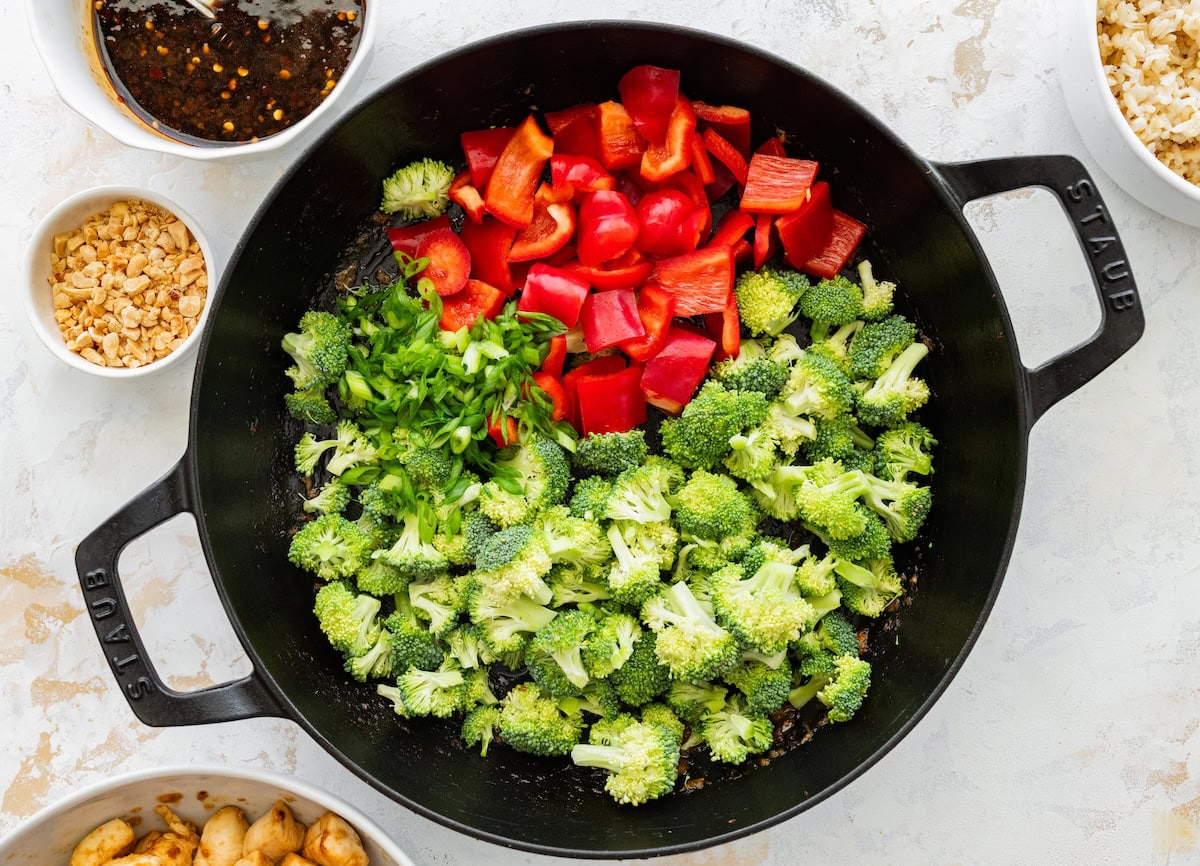 Chopped bell peppers and broccoli cooking together in a large skillet.
