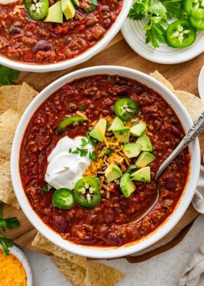 A bowl of slow cooked bean and beef chili topped with avocado, cheese, sour cream, and jalapeno slices.