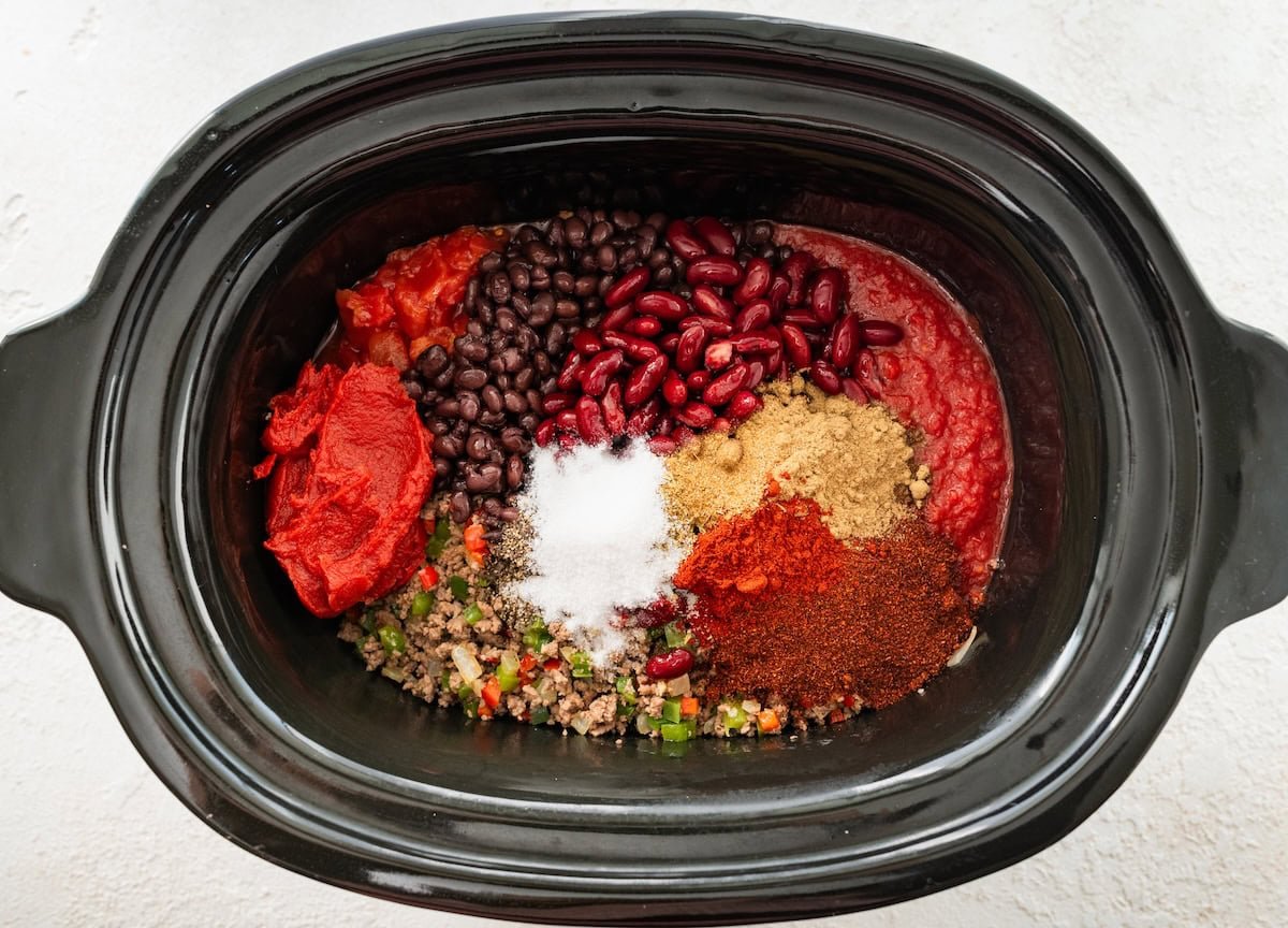 Black beans, kidney beans, tomato paste, diced tomatoes, ground beef, veggies, herbs, and spices in a slow cooker.