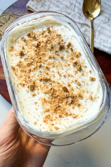 Yogurt cheesecake in a glass container topped with crushed cookies.