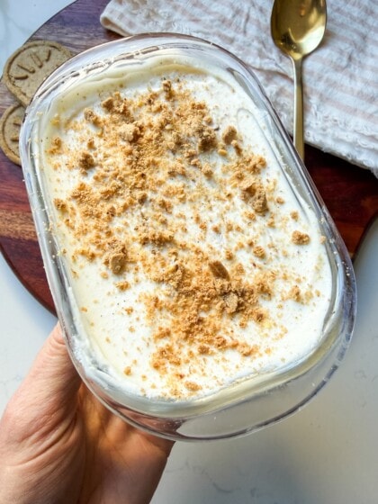 Yogurt cheesecake in a glass container topped with crushed cookies.