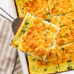 Slice of cottage cheese egg bake being removed from casserole dish with a spatula. Fresh herbs are on top.