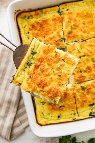 Slice of cottage cheese egg bake being removed from casserole dish with a spatula. Fresh herbs are on top.