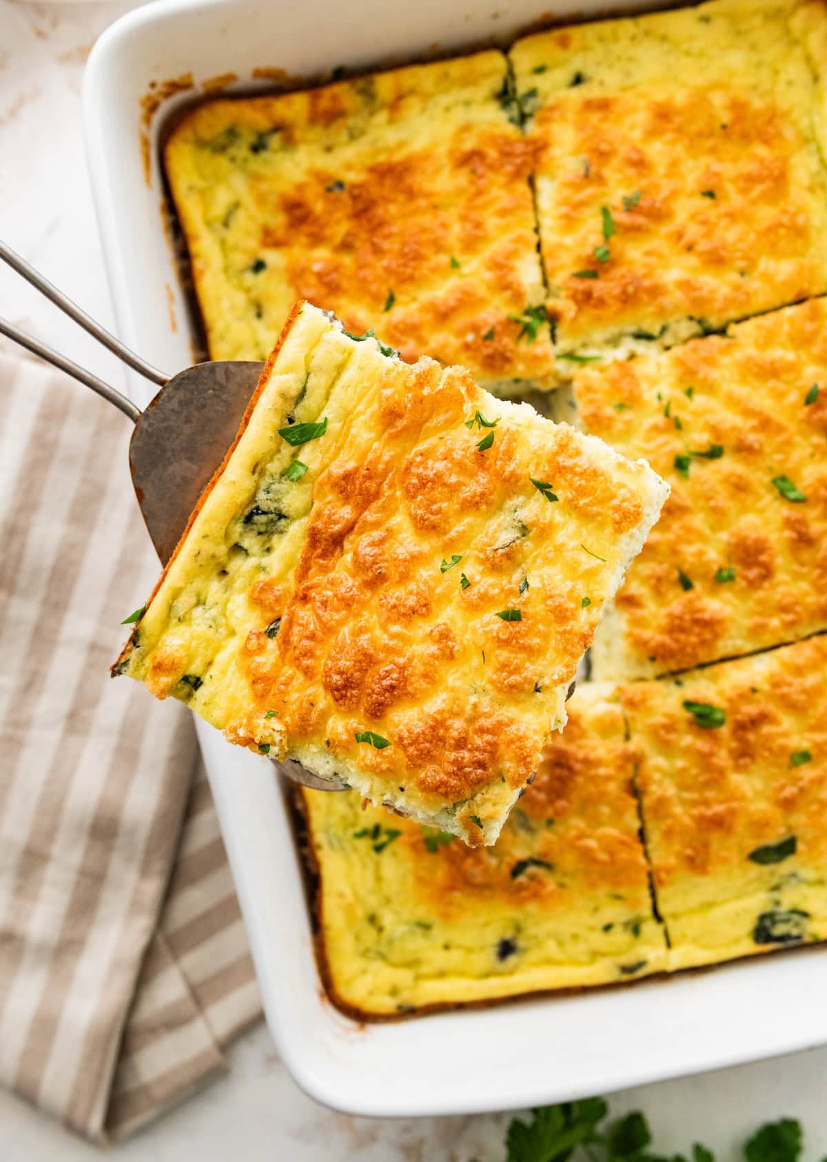 Slice of cottage cheese egg bake being removed from casserole dish with a spatula. Fresh herbs are on top.