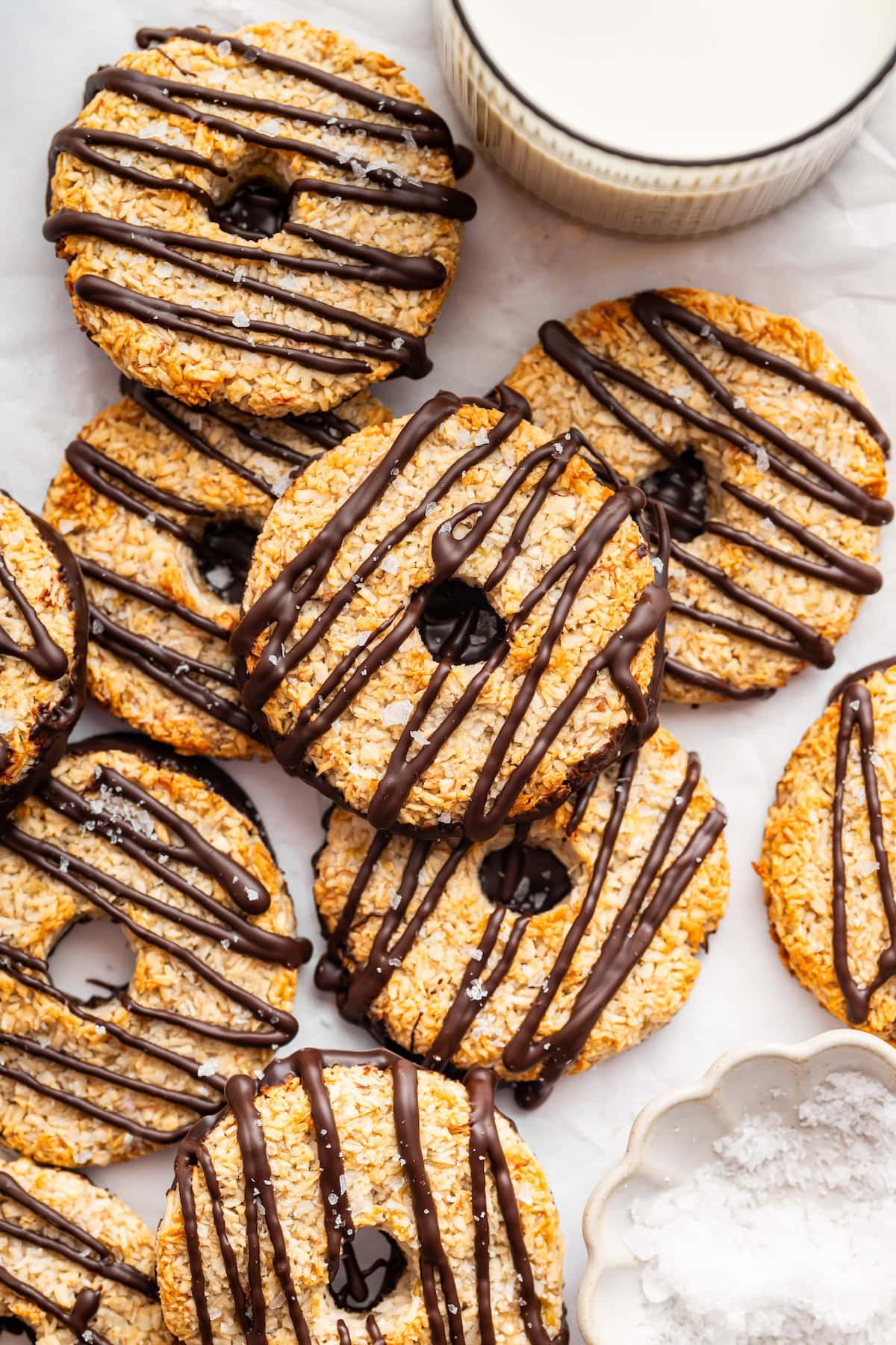 Banana samoas cookies spread out on a counter top near a glass of milk.