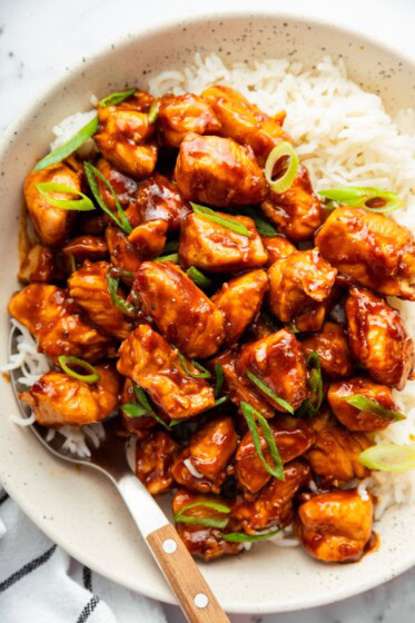 Sticky bourbon chicken garnished with green onions served over rice for an easy takeout-style dinner.