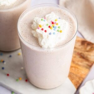 A cake batter protein shake in a glass topped with whipped cream and sprinkles.