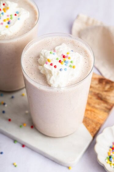 A cake batter protein shake in a glass topped with whipped cream and sprinkles.