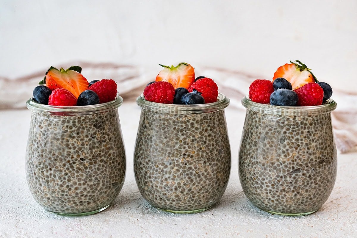 Three glass cups of chia pudding topped with fresh berries.
