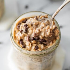 Cookie dough overnight oats topped with chocolate chips in a glass jar with a spoon in it.