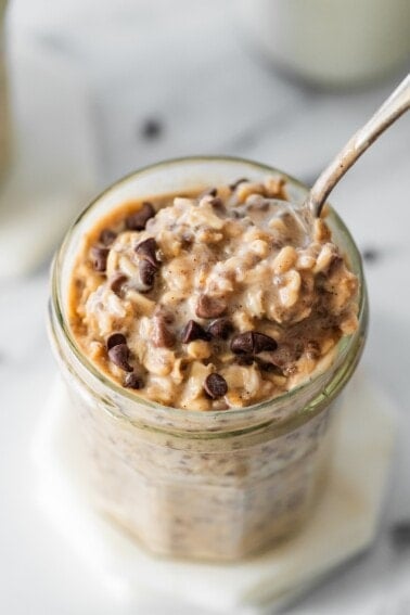 Cookie dough overnight oats topped with chocolate chips in a glass jar with a spoon in it.