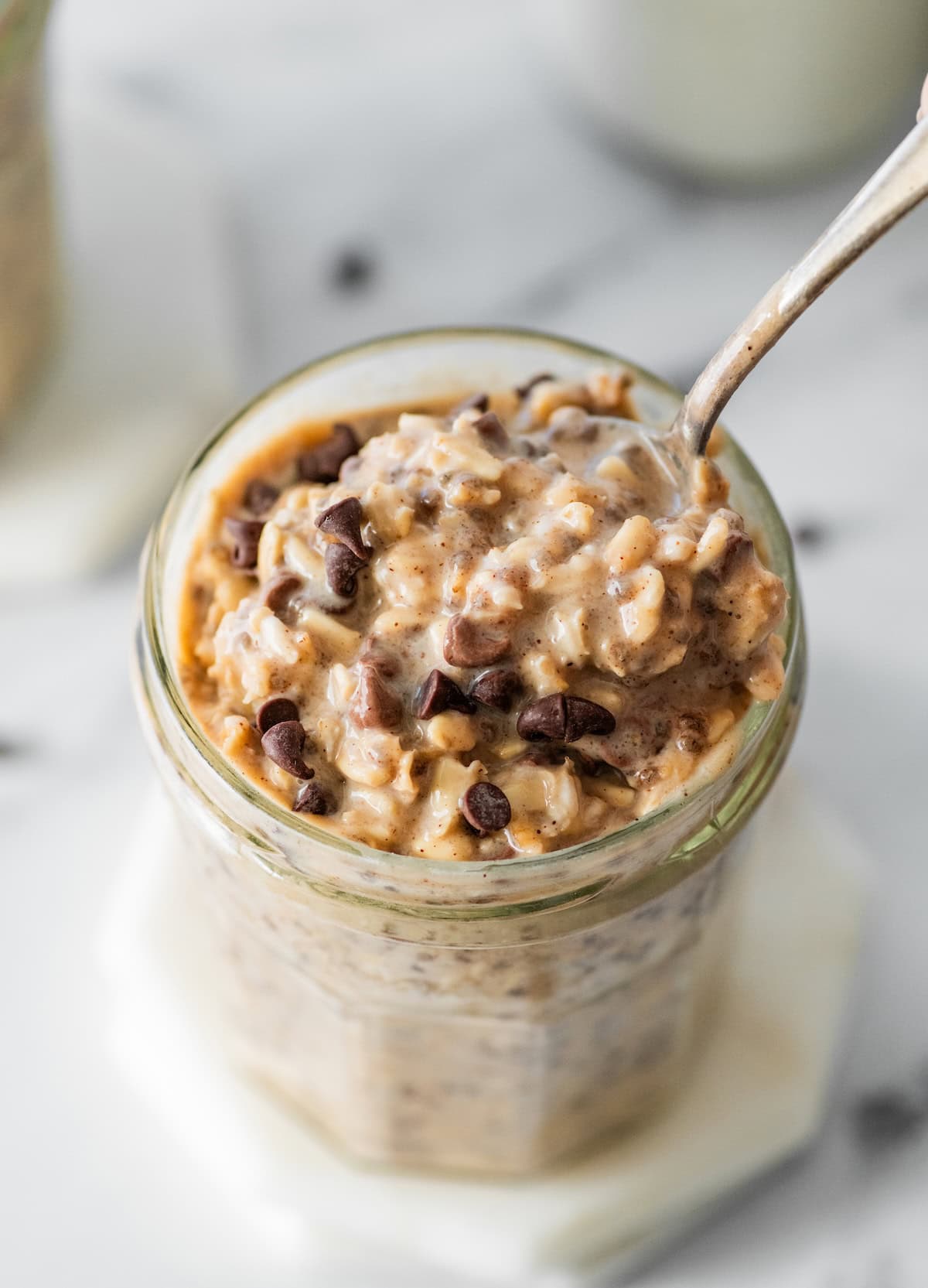 cookie dough overnight oats Cookie dough overnight oats topped with chocolate chips in a glass jar with a spoon in it.