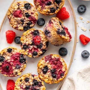 Cottage cheese baked oatmeal cups served on a platter. There are fresh blueberries and raspberries in the background.