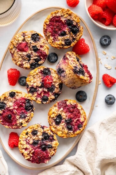 Cottage cheese baked oatmeal cups served on a platter. There are fresh blueberries and raspberries in the background.