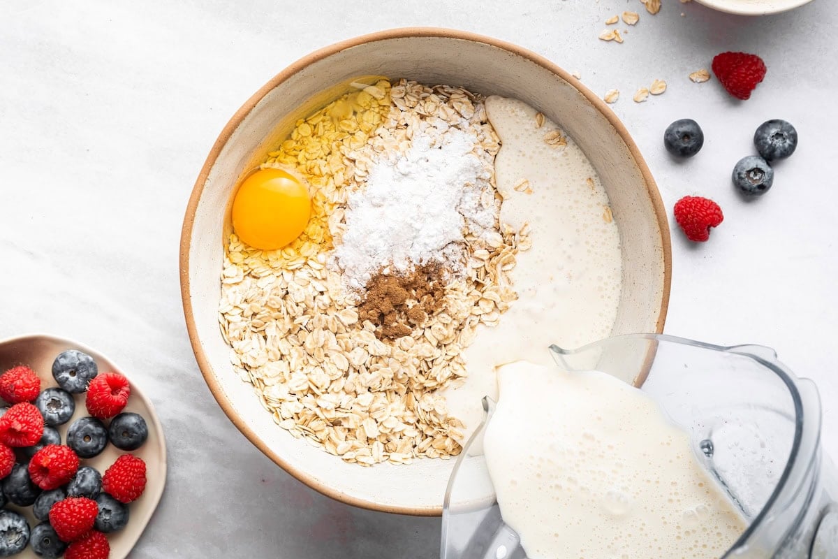 The wet ingredients being poured into the dry ingredients in a mixing bowl for the cottage cheese baked oatmeal cups.