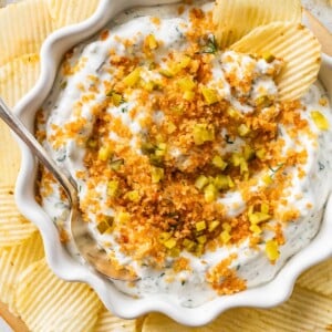 A serving of fried pickle dip in a bowl with multiple potato chips around the bowl.
