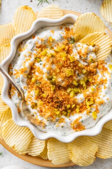 A serving of fried pickle dip in a bowl with multiple potato chips around the bowl.