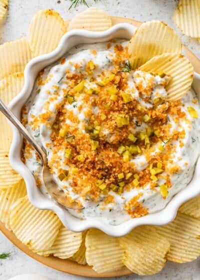 A serving of fried pickle dip in a bowl with multiple potato chips around the bowl.