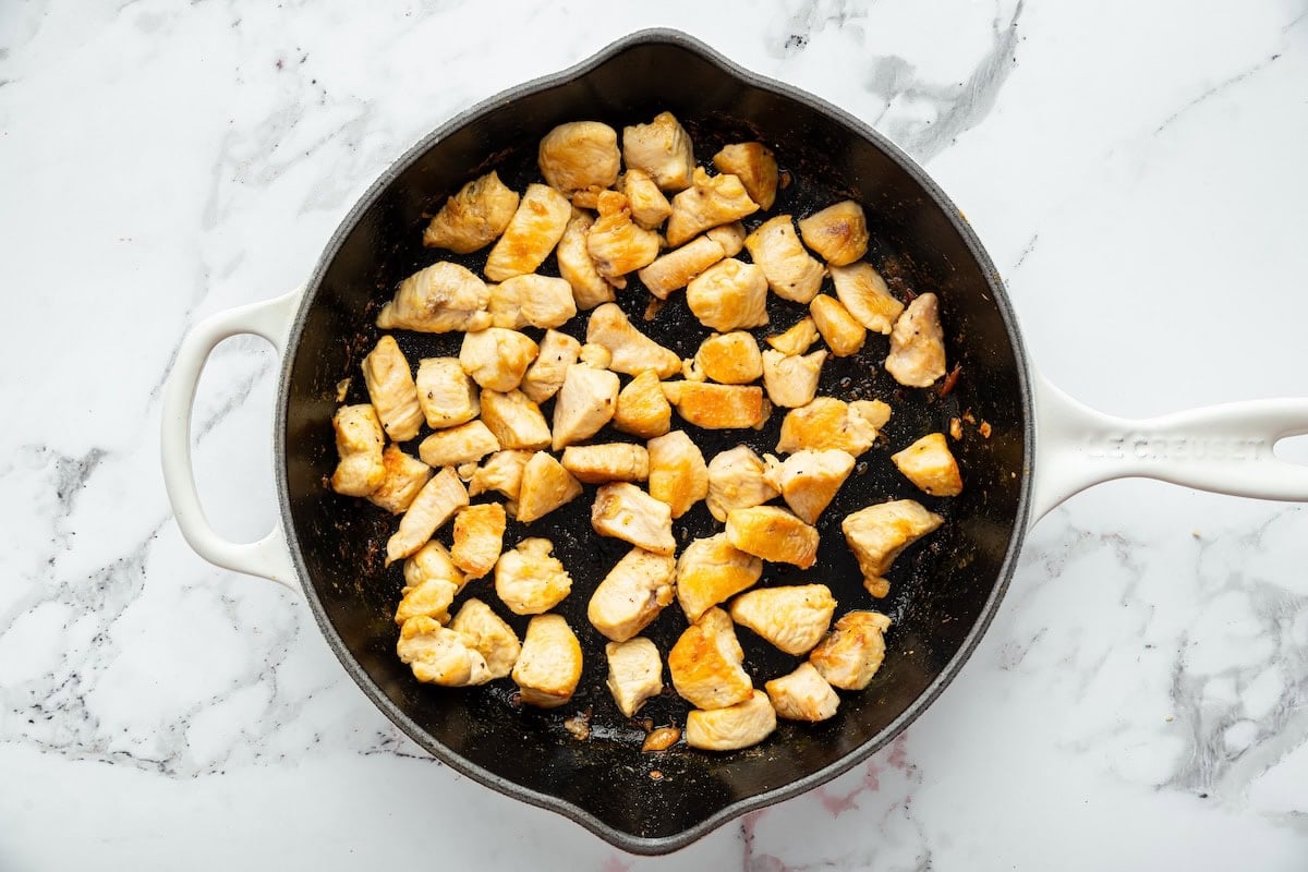 Chicken simmering in a sticky sweet and savory sauce as chicken thickens in skillet.