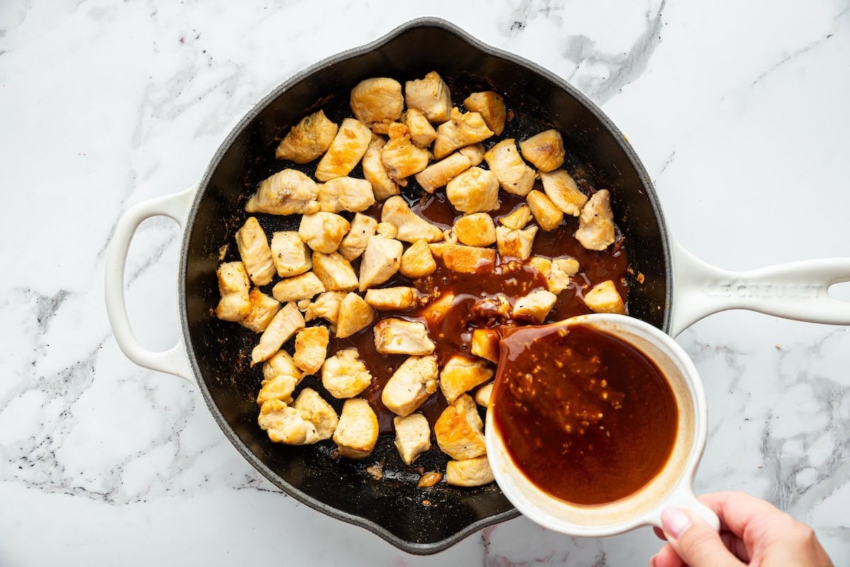 Sweet glazed chicken sauce being poured into skillet over cooked chicken pieces.