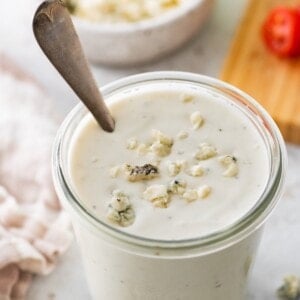 A glass jar of Greek yogurt blue cheese dressing with crumbled blue cheese pieces on top.