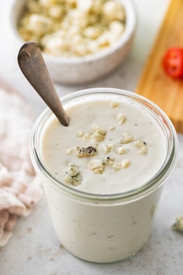 A glass jar of Greek yogurt blue cheese dressing with crumbled blue cheese pieces on top.
