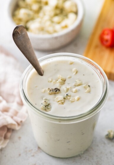 A glass jar of Greek yogurt blue cheese dressing with crumbled blue cheese pieces on top.