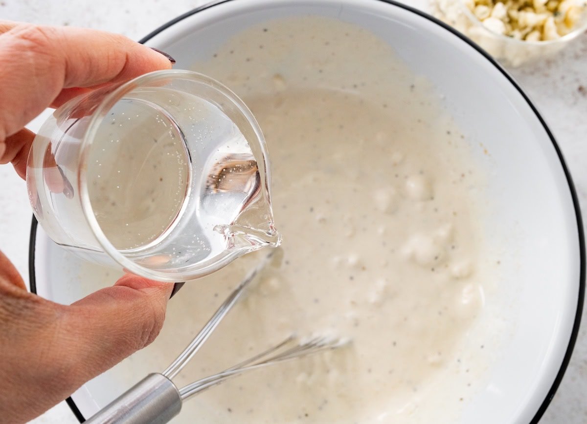 Water being poured into a mixing bowl of greek yogurt blue cheese dressing.