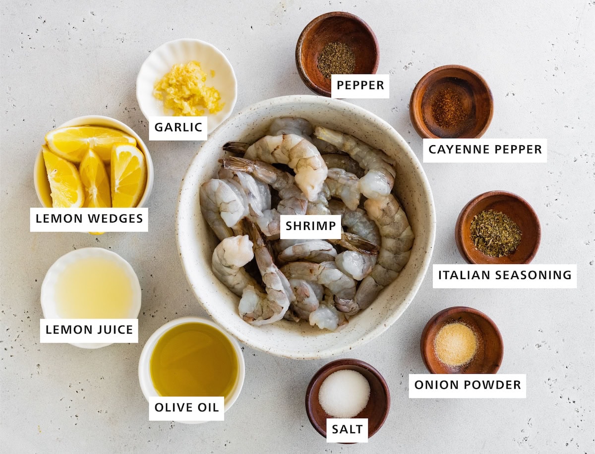 Ingredients measured out to make grilled shrimp: salt, pepper, cayenne pepper, lemon, onion powder, Italian seasoning, shrimp, garlic and olive oil.