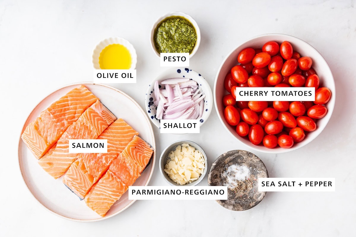 Ingredients measured out to make Pesto Salmon: salmon, olive oil, shallot, pesto, parmigiano-reggiano, sea salt, pepper and cherry tomatoes.