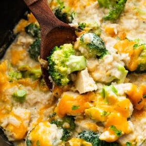 Chicken, rice, cheddar cheese, and broccoli in a slow cooker with a wooden serving spoon.