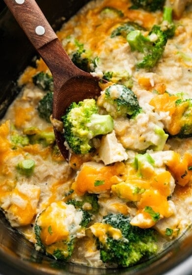 Chicken, rice, cheddar cheese, and broccoli in a slow cooker with a wooden serving spoon.