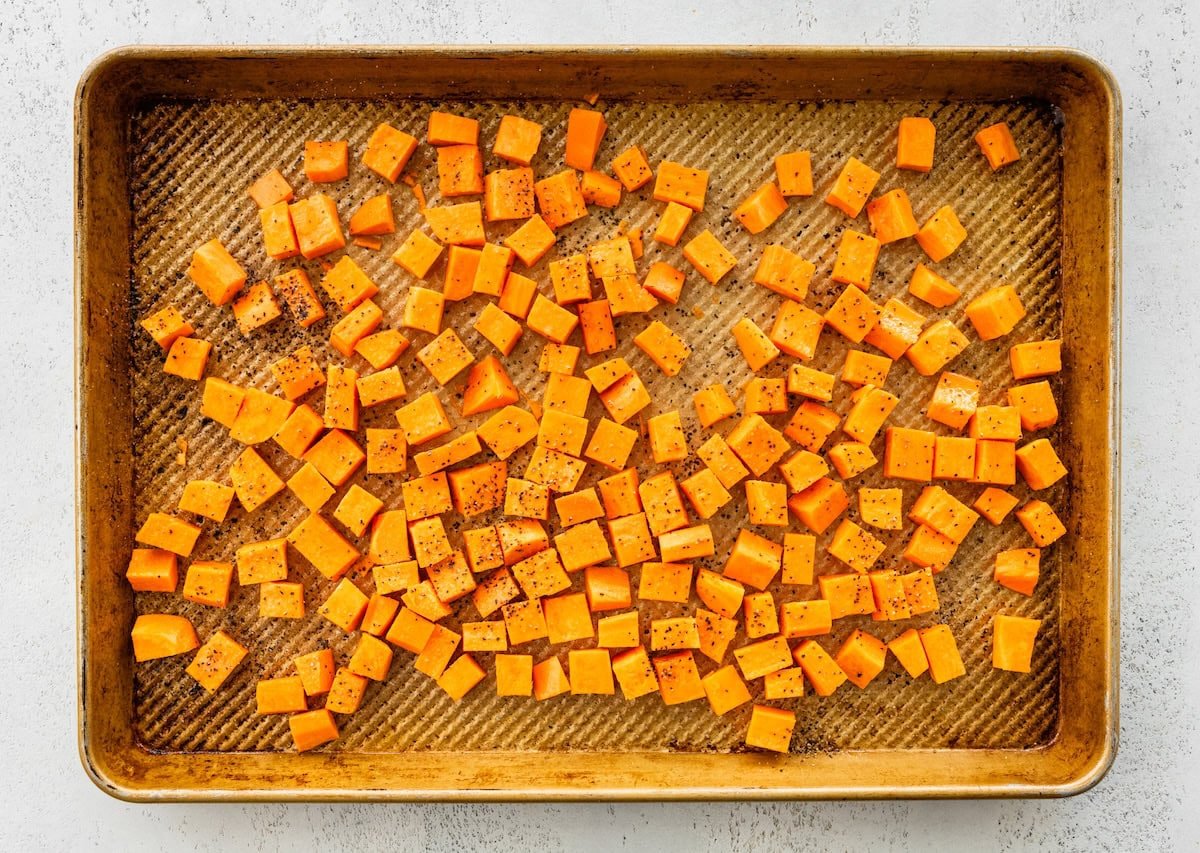 A baking tray with diced and seasoned sweet potato.