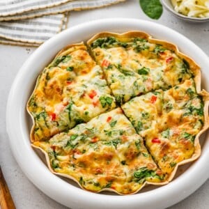 Single-serve tortilla quiche sliced into wedges showing spinach, peppers, and cheesy egg filling.