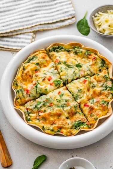 Single-serve tortilla quiche sliced into wedges showing spinach, peppers, and cheesy egg filling.