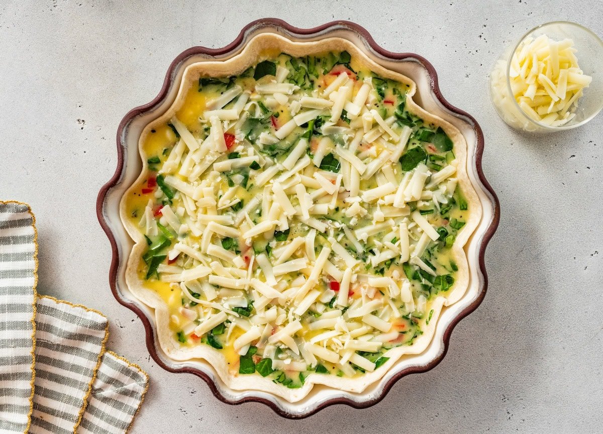 Tortilla quiche crust filled with spinach, peppers, and shredded cheese before baking.
