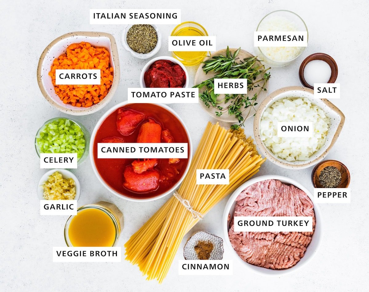 Ingredients measured out to make Turkey Bolognese: veggie broth, garlic, celery, carrots, Italian seasoning, canned tomatoes, tomato paste, cinnamon, pasta, herbs, olive oil, ground turkey, yellow onion, parmesan, salt and pepper.