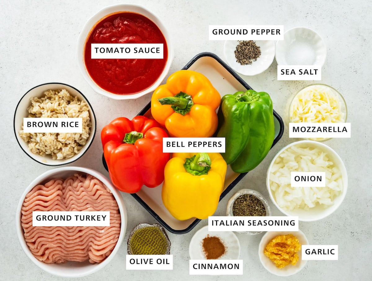 Ingredients for turkey stuffed peppers including bell peppers, ground turkey, grown rice, tomato sauce, ground pepper, sea salt, mozzarella, onion, italian seasoning, garlic, cinnamon, and olive oil.