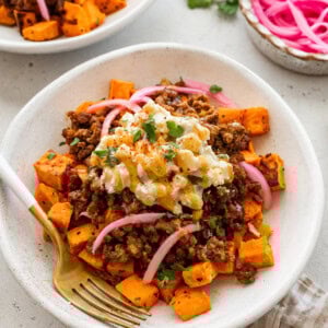 A bed of roasted sweet potatoes topped with ground beef, a creamy street corn salsa, pickled red onions, cilantro and a drizzle of hot honey.