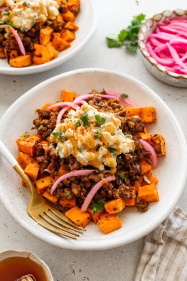 A bed of roasted sweet potatoes topped with ground beef, a creamy street corn salsa, pickled red onions, cilantro and a drizzle of hot honey.
