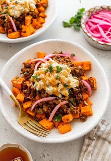 A bed of roasted sweet potatoes topped with ground beef, a creamy street corn salsa, pickled red onions, cilantro and a drizzle of hot honey.