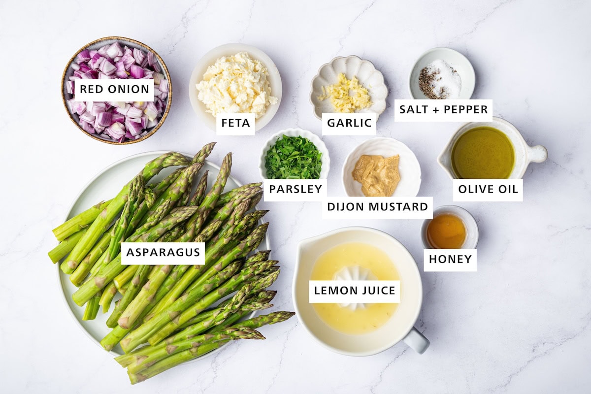 Ingredients measured out to make Asparagus Salad with Lemon and Feta: Asparagus, red onion, feta, parsley, garlic, lemon juice, Dijon mustard, honey, olive oil, salt, pepper.