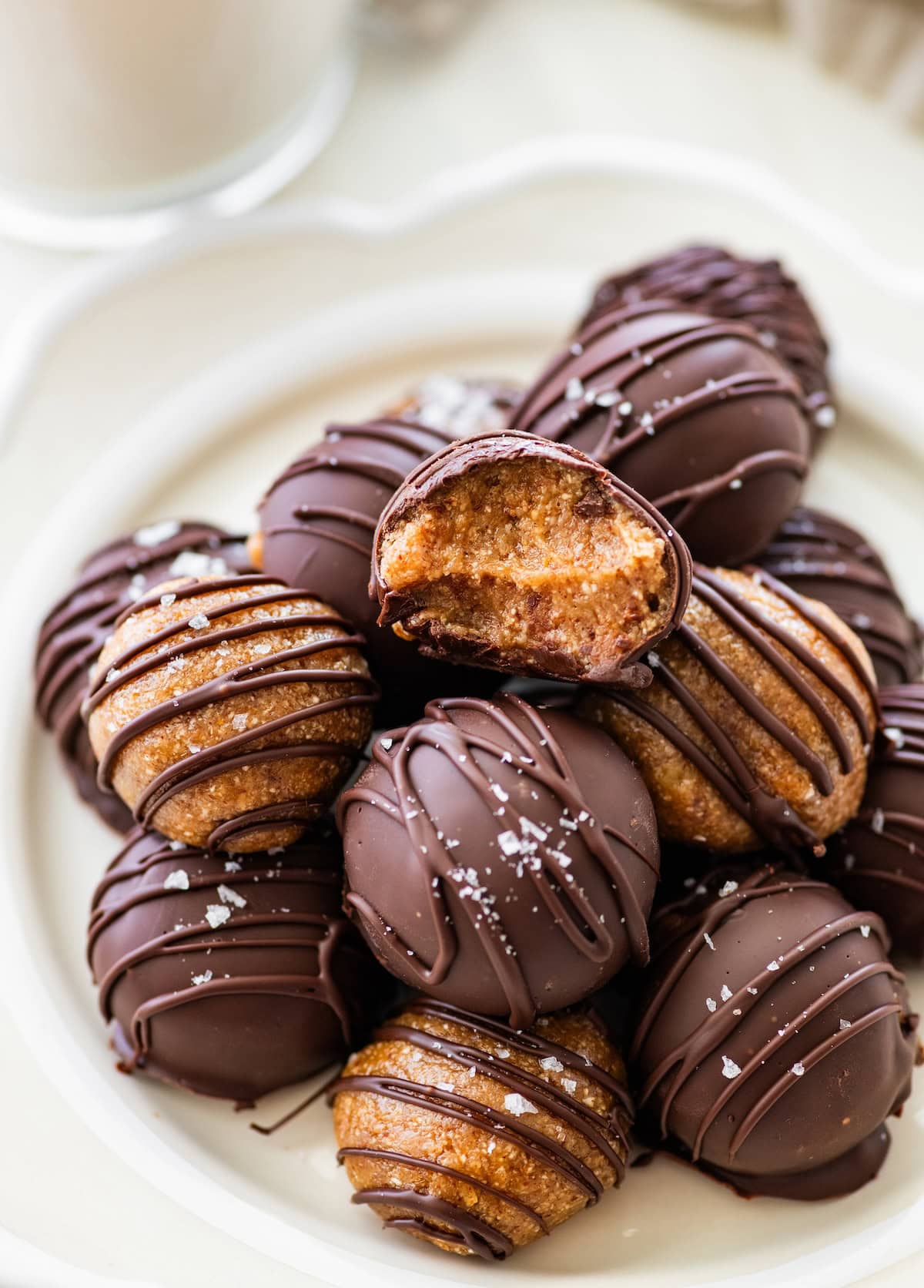 Banana bread protein balls served on a plate. Half of the balls are dipped in chocolate and half are drizzled with chocolate. The top protein ball has a bite taken out of it.