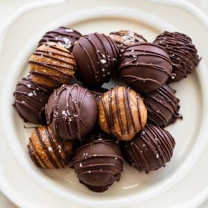Banana bread protein balls on a plate. Half are dipped in chocolate and half are drizzled with chocolate.