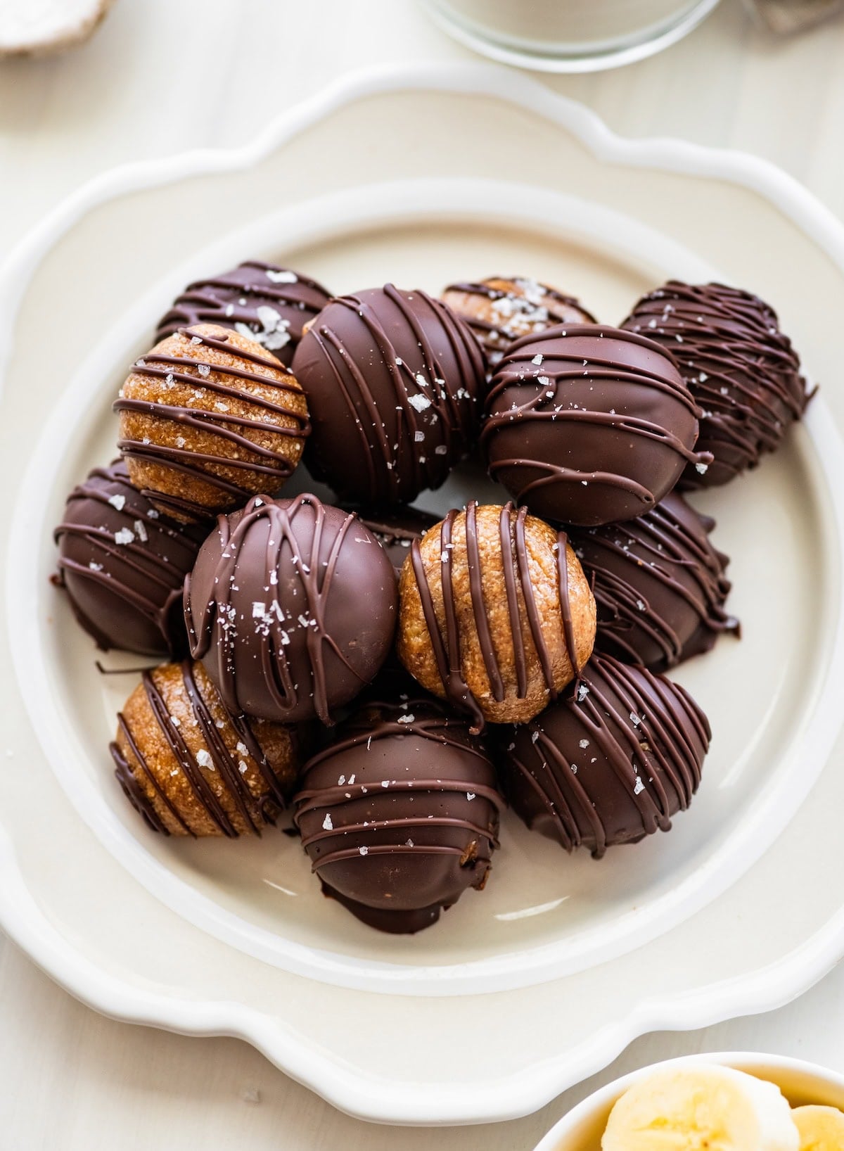 Banana bread protein balls on a plate. Half are dipped in chocolate and half are drizzled with chocolate.